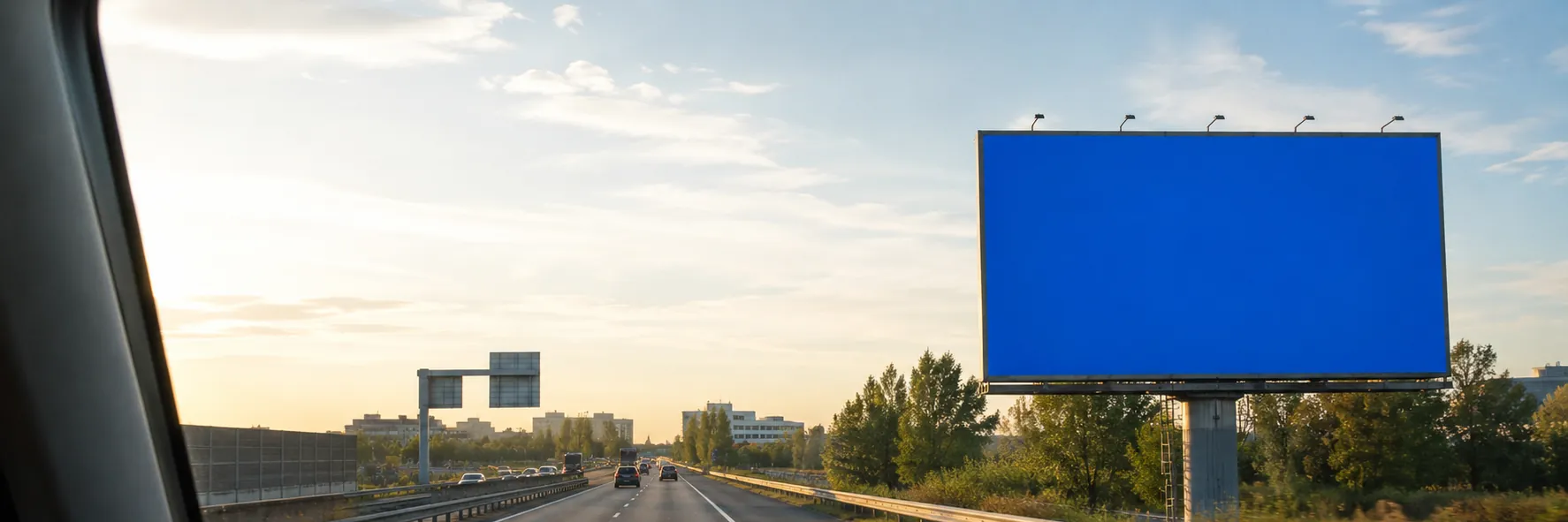 Panneau publicitaire au bord d'une autoroute d'Île-de-France, vu depuis le poste de conduite d'un utilitaire au coucher du soleil